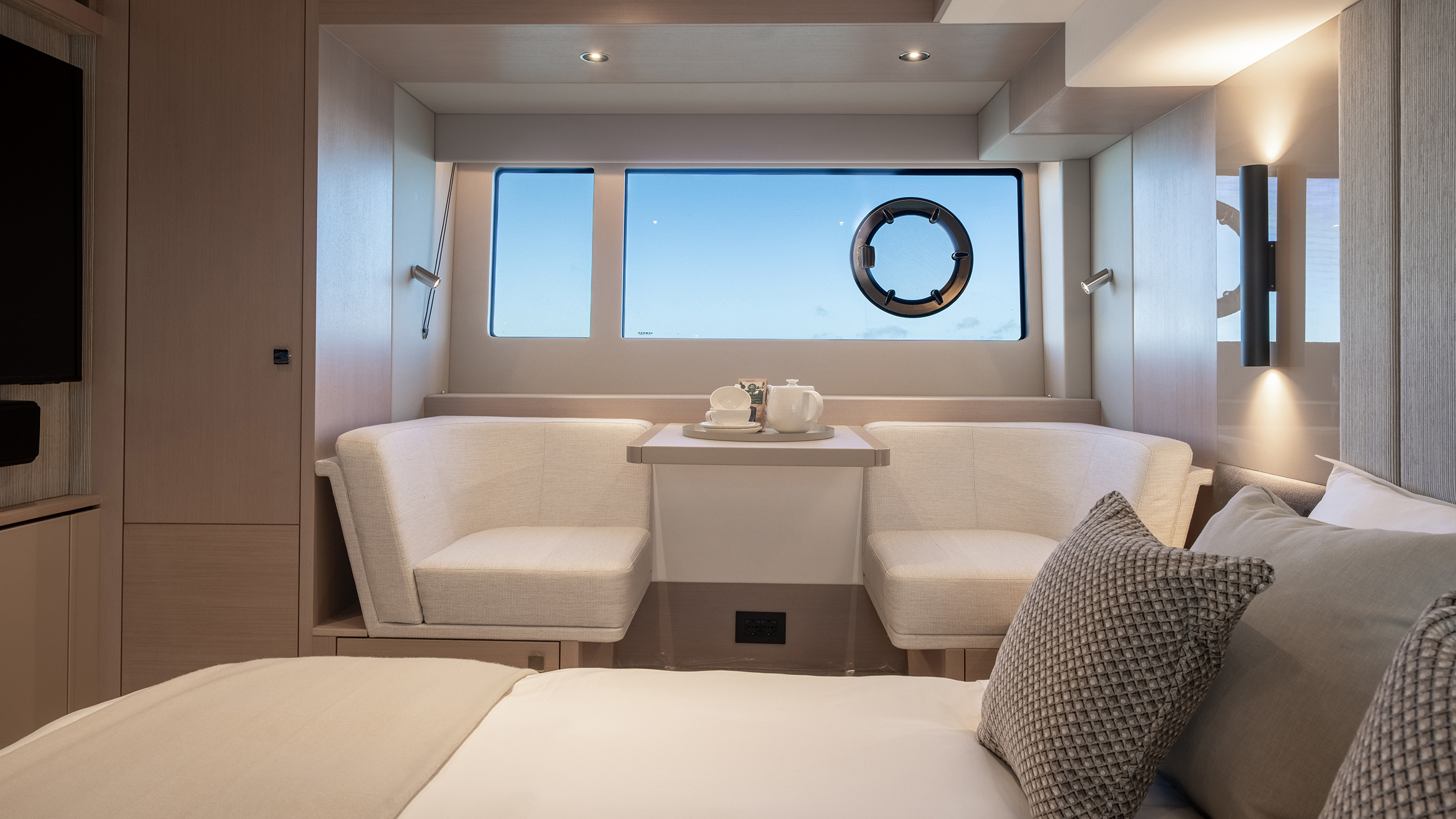 Sunseeker Manhattan 56 — master cabin sitting area, curved twin sofas, porthole, dusk sky