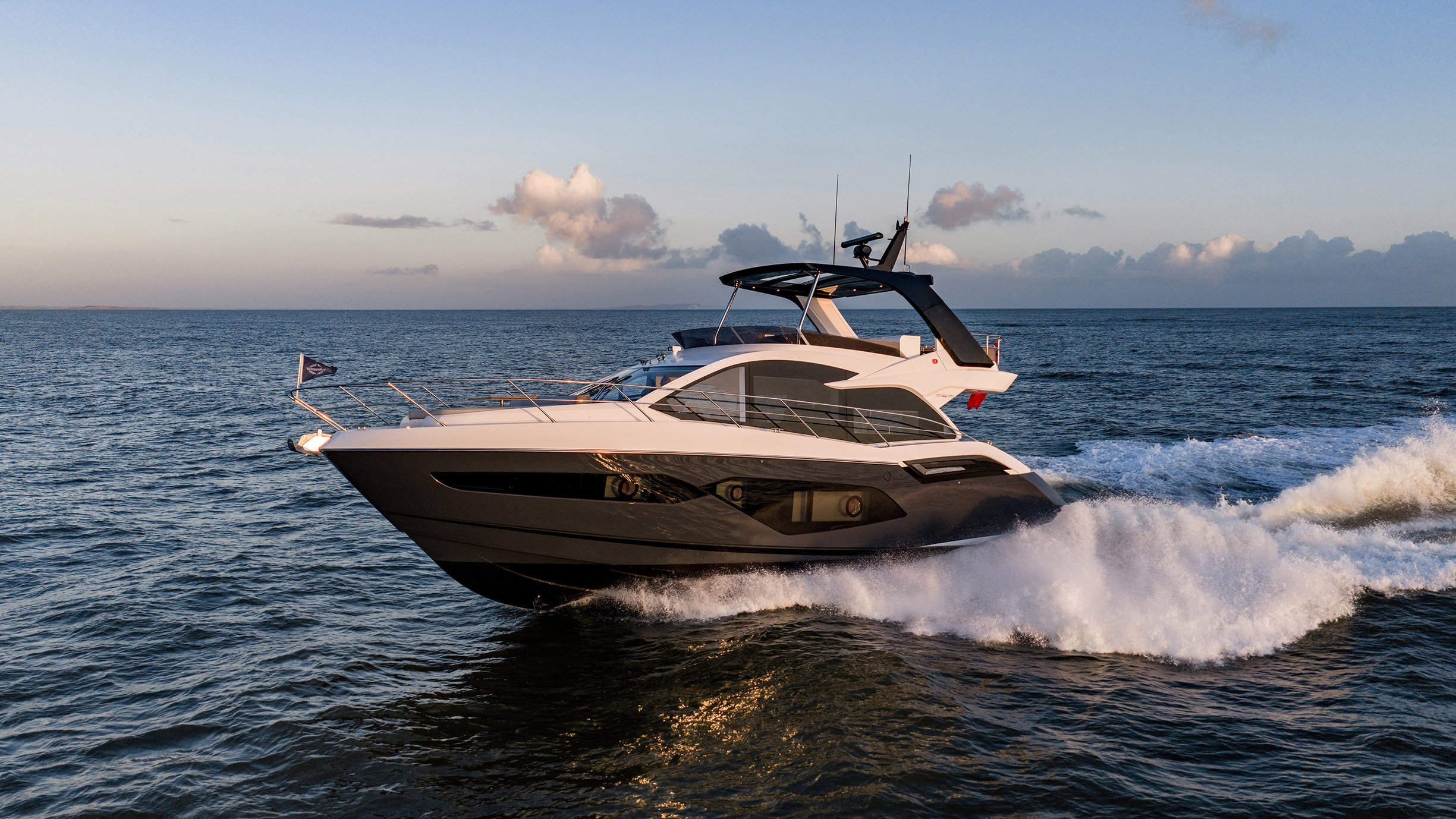 Sunseeker Manhattan 56 — port bow running at speed, golden hour, Dorset coast, white and dark hull