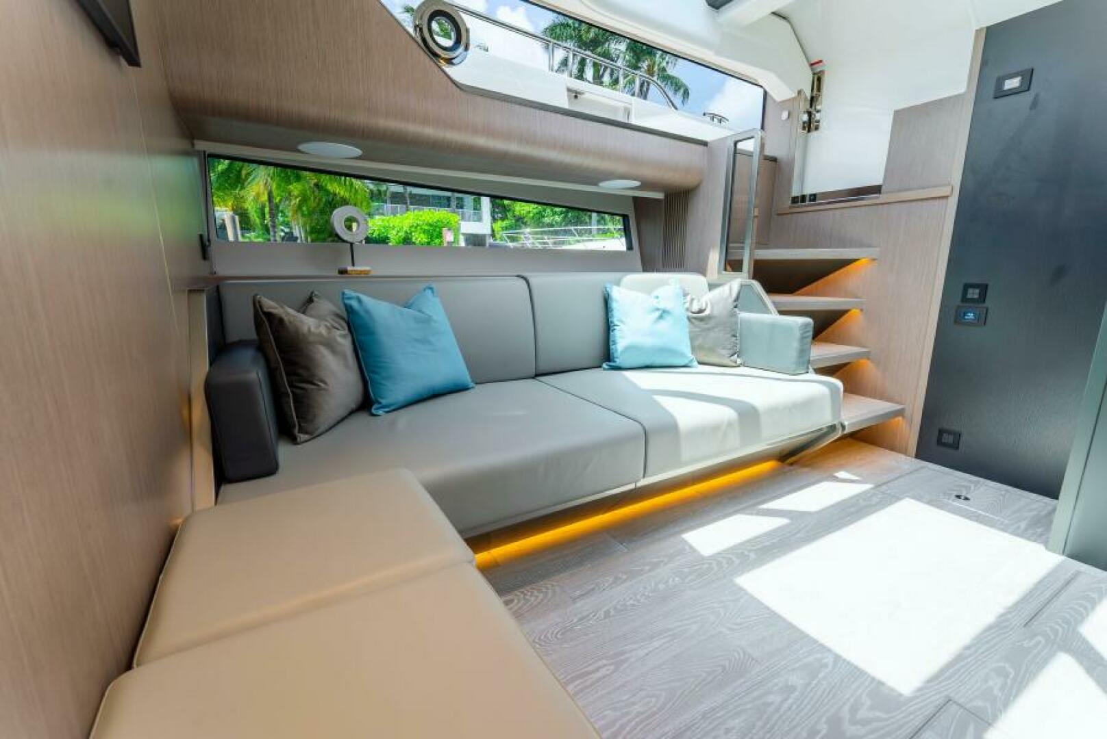 Sunseeker Superhawk 55 — saloon sofa with teal accent pillows, ambient LED undertow, staircase to deck